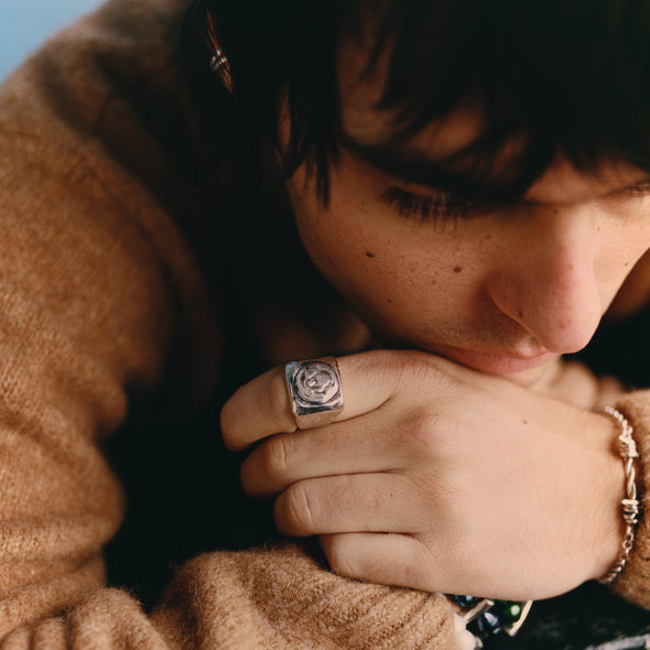 Person wearing a brown sweater with a ring and bracelet, resting their head on their hand.