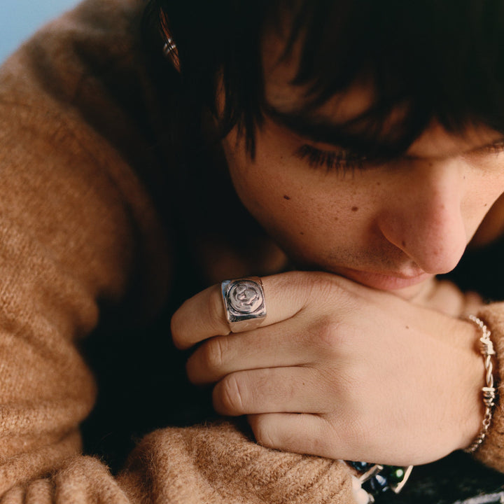 Person wearing a brown sweater with a ring and bracelet, resting their head on their hand.