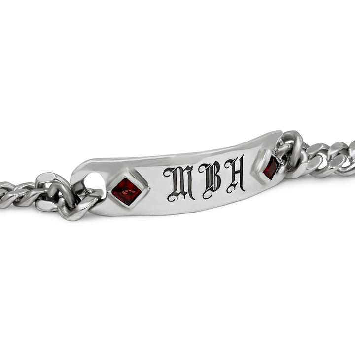 Silver bracelet with engraved initials and red stones on a white background