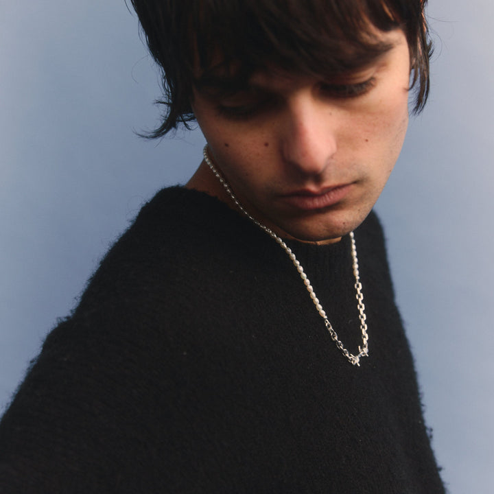 Person wearing a black sweater and chain necklace against a plain background