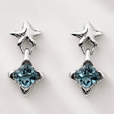 A pair of silver-toned dangle earrings featuring a small star-shaped stud at the top and a larger faceted star drop with a light blue gemstone at the bottom, set against a plain light background.