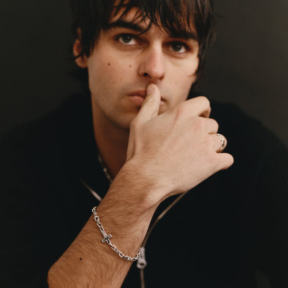 Man with hand on chin wearing a silver bracelet and ring against a dark background