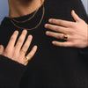 Person wearing gold necklaces and rings on a plain background