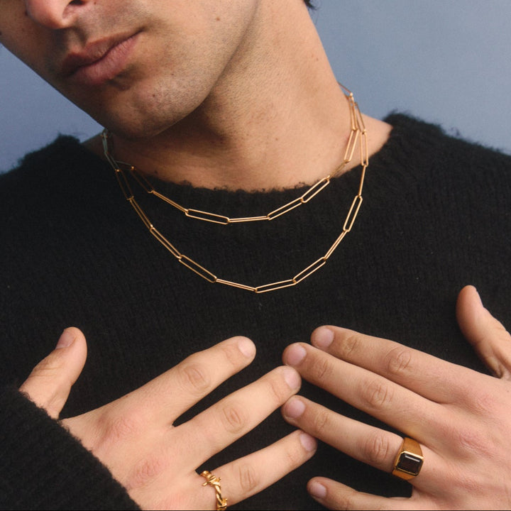 Man wearing a gold necklace and rings against a blue background
