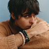Person wearing a brown sweater with bracelets on a neutral background
