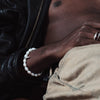 A person wearing a black leather jacket and beige pants, with a white pearl spike bracelet on their wrist.