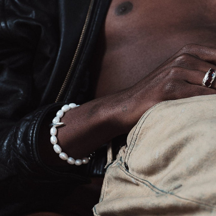 A person wearing a black leather jacket and beige pants, with a white pearl spike bracelet on their wrist.