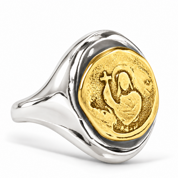 A silver signet ring featuring a round gold-toned medallion with an embossed religious figure and cross, shown on a clean white background.