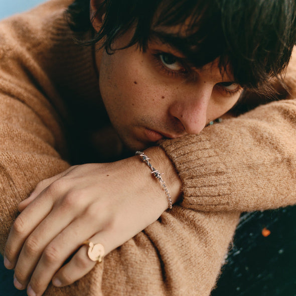 Person wearing a brown sweater with a close-up of their hand and jewelry.