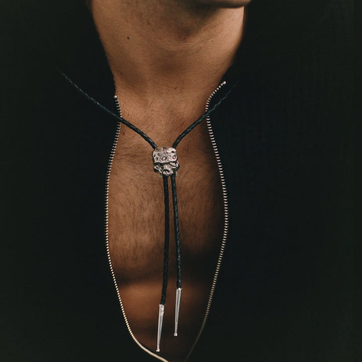 Close-up of a person wearing a black bolo tie with a silver clasp.