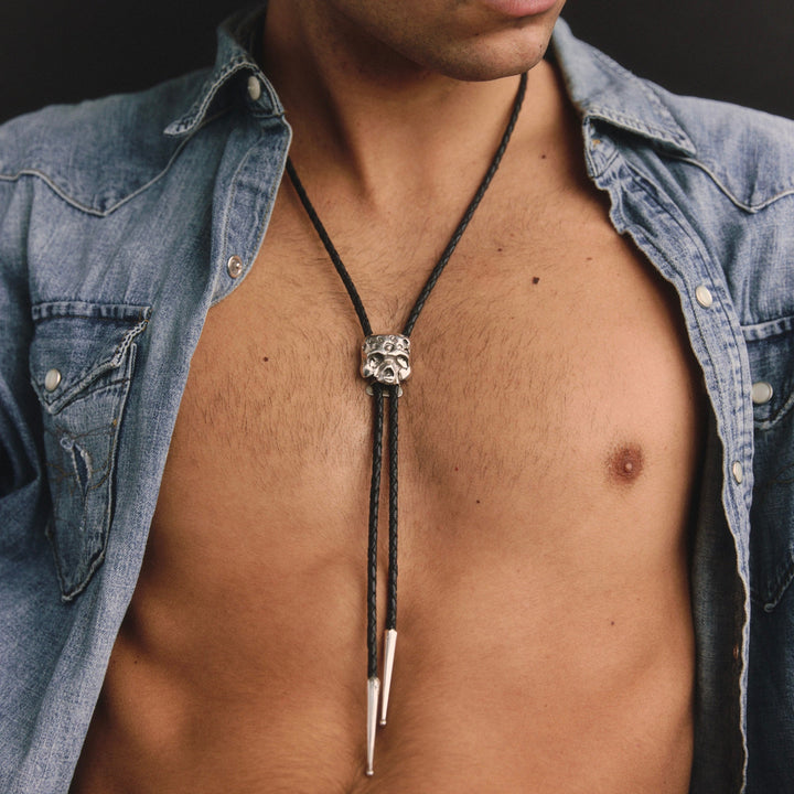 Man wearing a denim shirt with a bolo tie, shirt open to reveal chest.