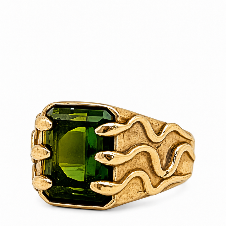 A gold signet ring featuring a large, rectangular emerald-cut green gemstone and a textured, flame-like gold band, shown on a plain white background.