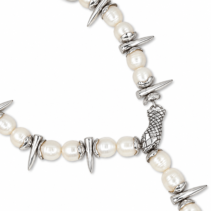 A close-up of a pearl and silver necklace featuring white pearl beads, silver spike charms, and a textured silver mermaid tail charm on a white background.