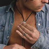 Man wearing a denim shirt with visible jewelry, including rings and a necklace.
