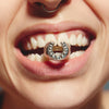 Close-up of a mouth with a decorative ring on a tooth against a neutral background
