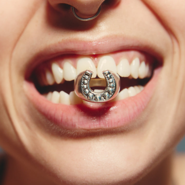 Close-up of a mouth with a decorative ring on a tooth against a neutral background