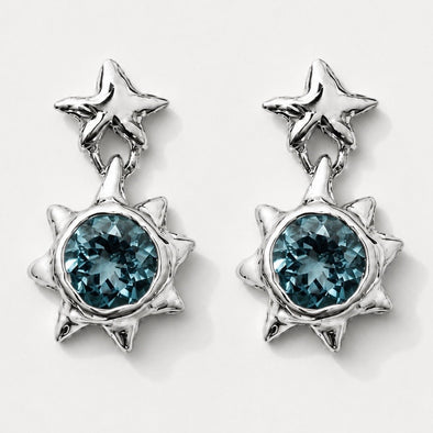 A pair of silver-toned dangle earrings featuring a small star-shaped stud at the top and a larger spiky sunburst pendant with a faceted blue-green gemstone in the center, shown on a light gray background.