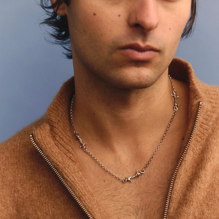 Man wearing a brown zip-up sweater with a necklace against a blue background