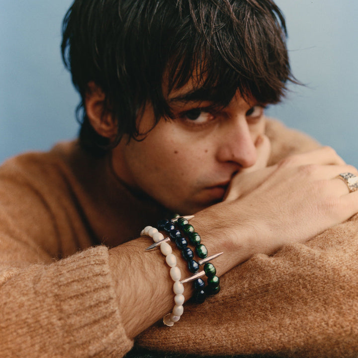 Person wearing a brown sweater with bracelets on a light blue background