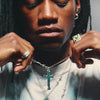 A person with a close-up on their neck, wearing a silver-colored cross-shaped pendant on a barbed chain necklace.