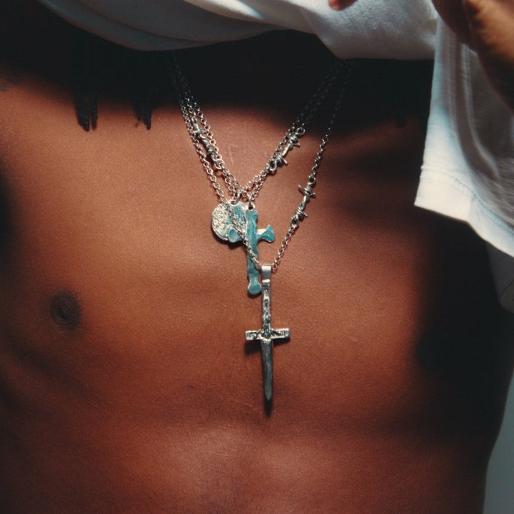 A sterling silver cross pendant necklace with a hammered finish on a heavy Rolo chain featuring a single barbed wire link.