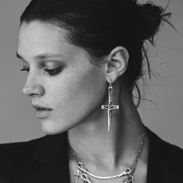 Black and white portrait of a woman wearing earrings and a necklace against a plain background