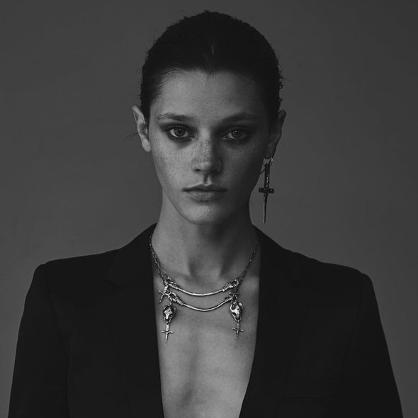 Black and white portrait of a person wearing a dark blazer and layered necklaces.