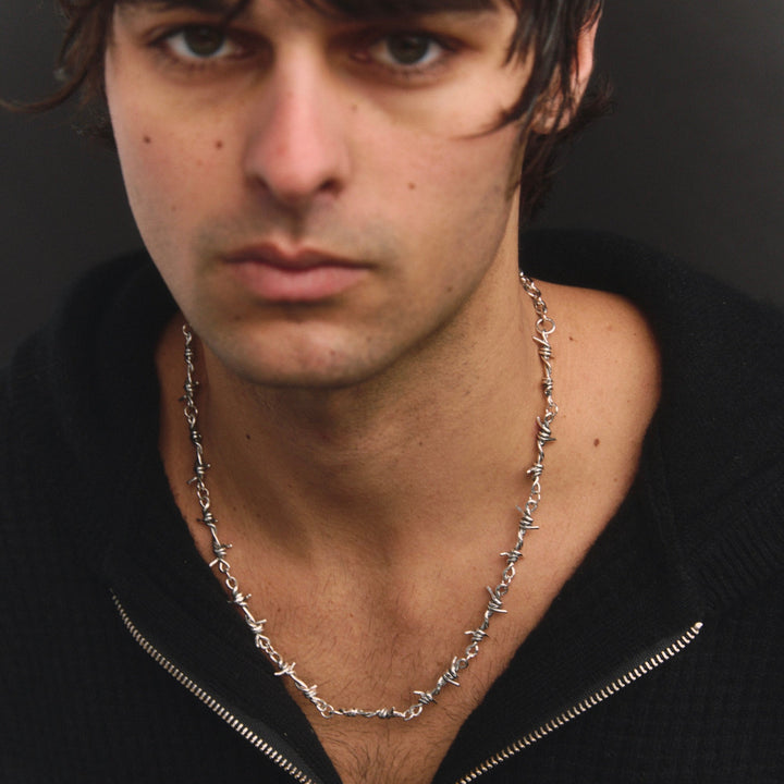 Man wearing a black zip-up hoodie and silver chain necklace against a dark background