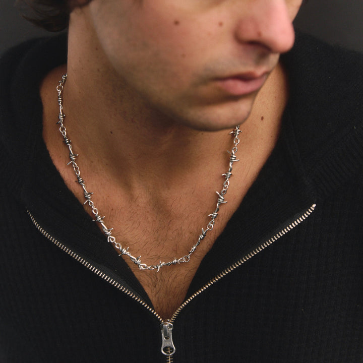 Man wearing a black sweater and silver necklace against a dark background
