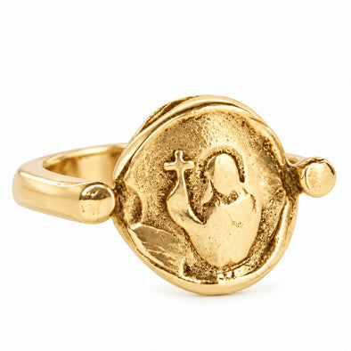 A gold-toned ring featuring a textured, circular medallion with a raised figure holding a cross, photographed on a clean white background.