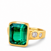 A yellow gold ring featuring a large rectangular emerald-cut green gemstone and two small round clear stones on the band, set against a plain white background.