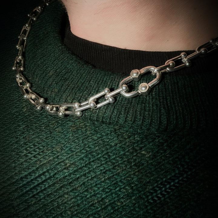 Close-up of a chain necklace on a person wearing a green sweater.