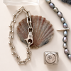 Silver chain bracelet with clasp, shell, and beaded necklace on a white surface