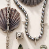 Jewelry set with pearls, silver chain, and shell elements on a light background