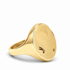 A polished yellow gold signet ring with a flat oval face featuring two small engraved marks, shown on a clean white background.