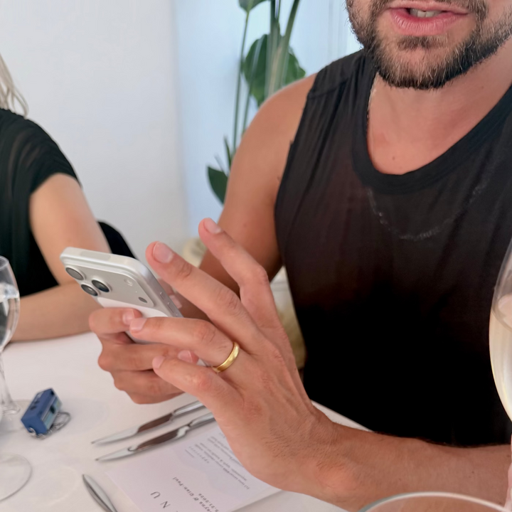 Man using a smartphone at a dining table with cutlery and glasses.