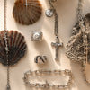 Silver jewelry including necklaces, rings, and a bracelet on a textured surface.
