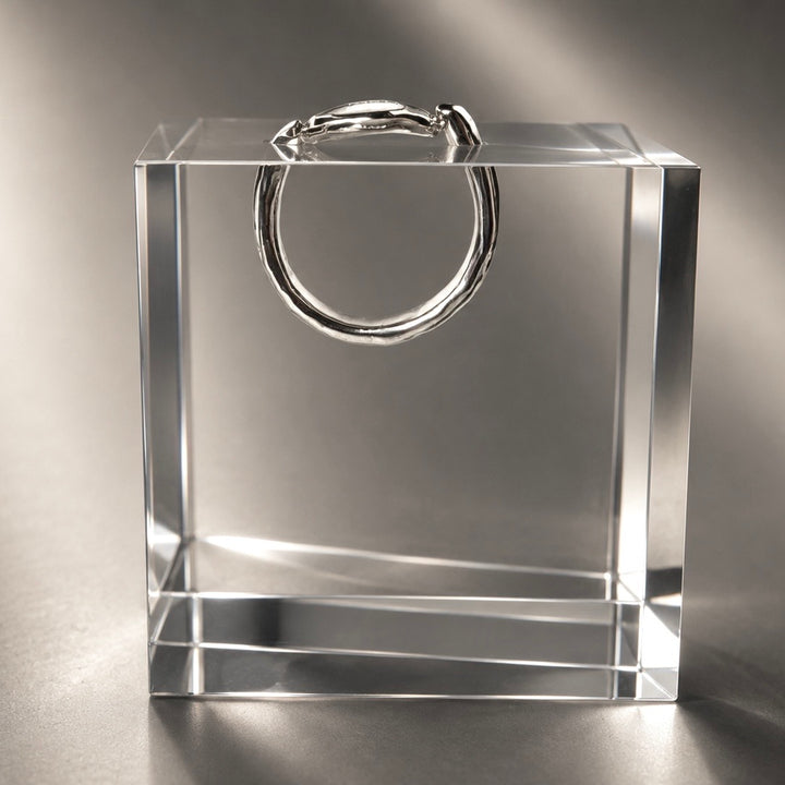A polished silver ring displayed inside a clear acrylic block on a reflective gray surface.