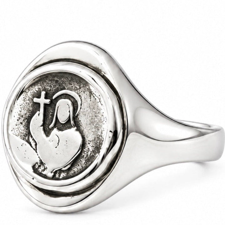 A sterling silver signet ring featuring an oxidized religious design of a heart with a cross and halo, set against a clean white background.