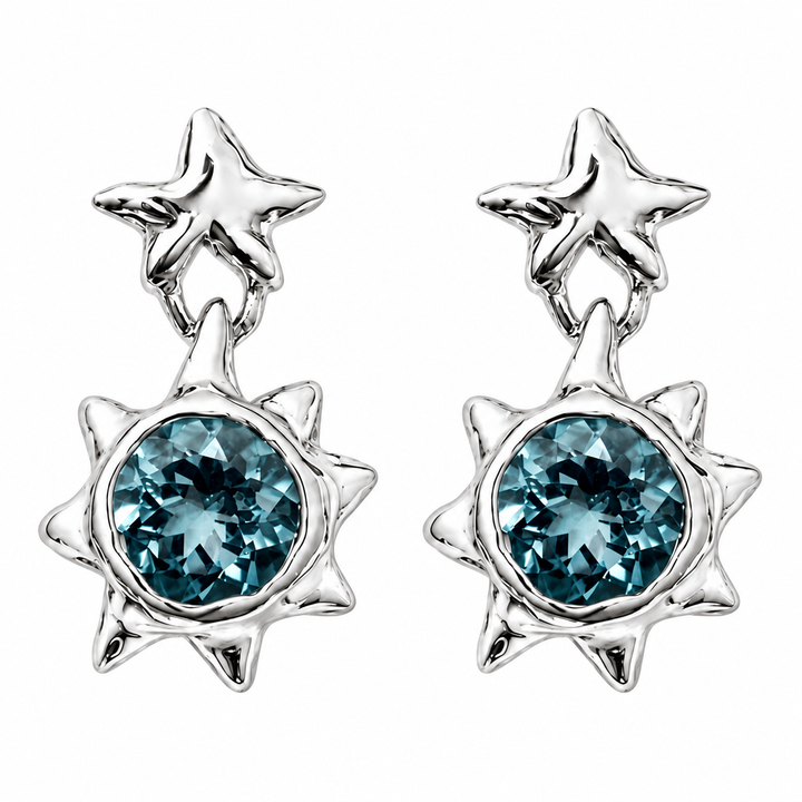A pair of silver starburst dangle earrings featuring round faceted blue gemstones, shown on a solid white background.