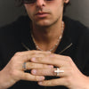 Person wearing two rings, one with a cross design, on a dark background