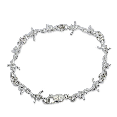 Silver bracelet with barbed wire shape laid over white background