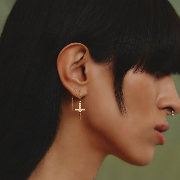 female model wearing our crucifix dagger threader earring with green background, pictured from her right side