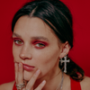 female model posing in red background with hand in her mouth, wearing our XL cross hoop earrings