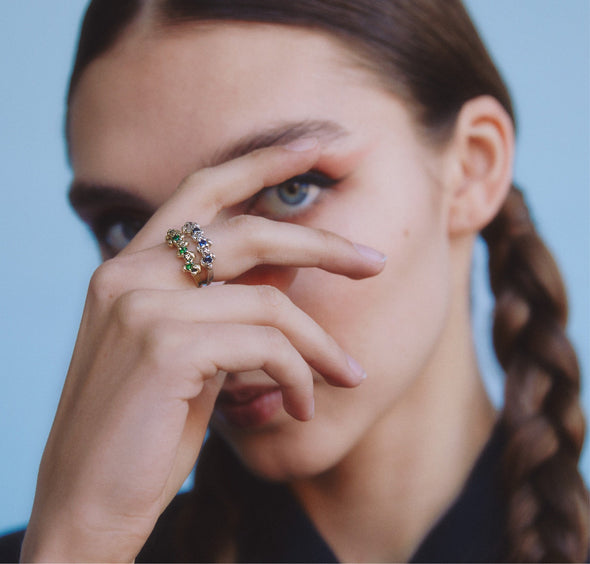 female model covering her face with her hand, wearing our studded sapphire and garnet rings